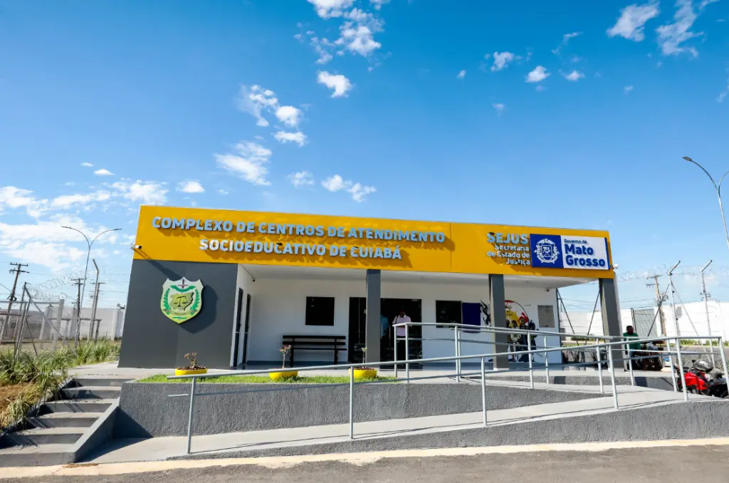 Vista frontal de um moderno complexo judiciário com fachada de vidro espelhado e estrutura branca. À frente, um amplo estacionamento e palmeiras sob um céu azul claro.