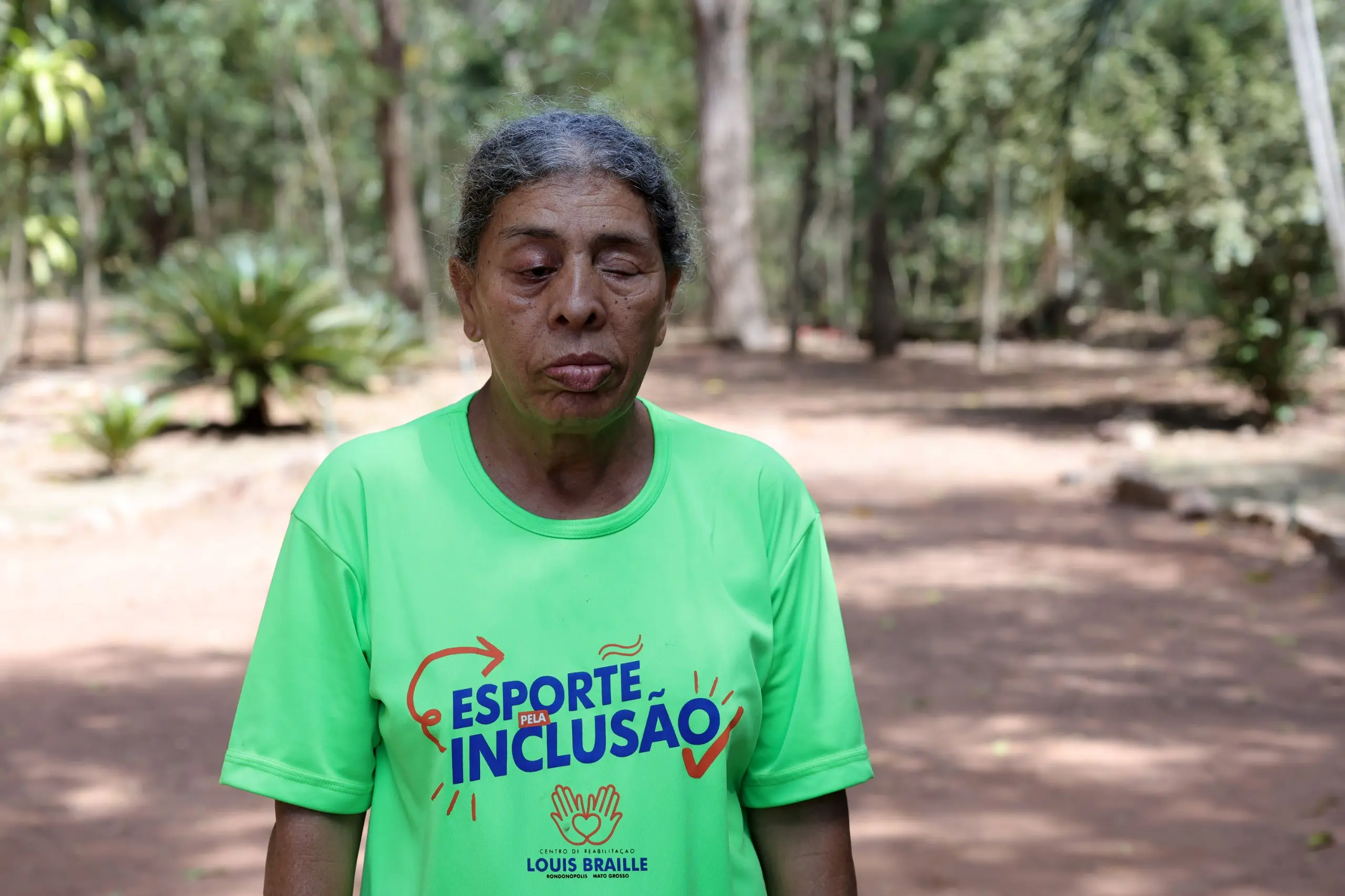 Mulher branca de cabelos longos e castanhos, batom vermelho e blazer vermelho sobre blusa clara. Ao fundo desfocado, uma projeção com texto em português começa com a palavra Correr.