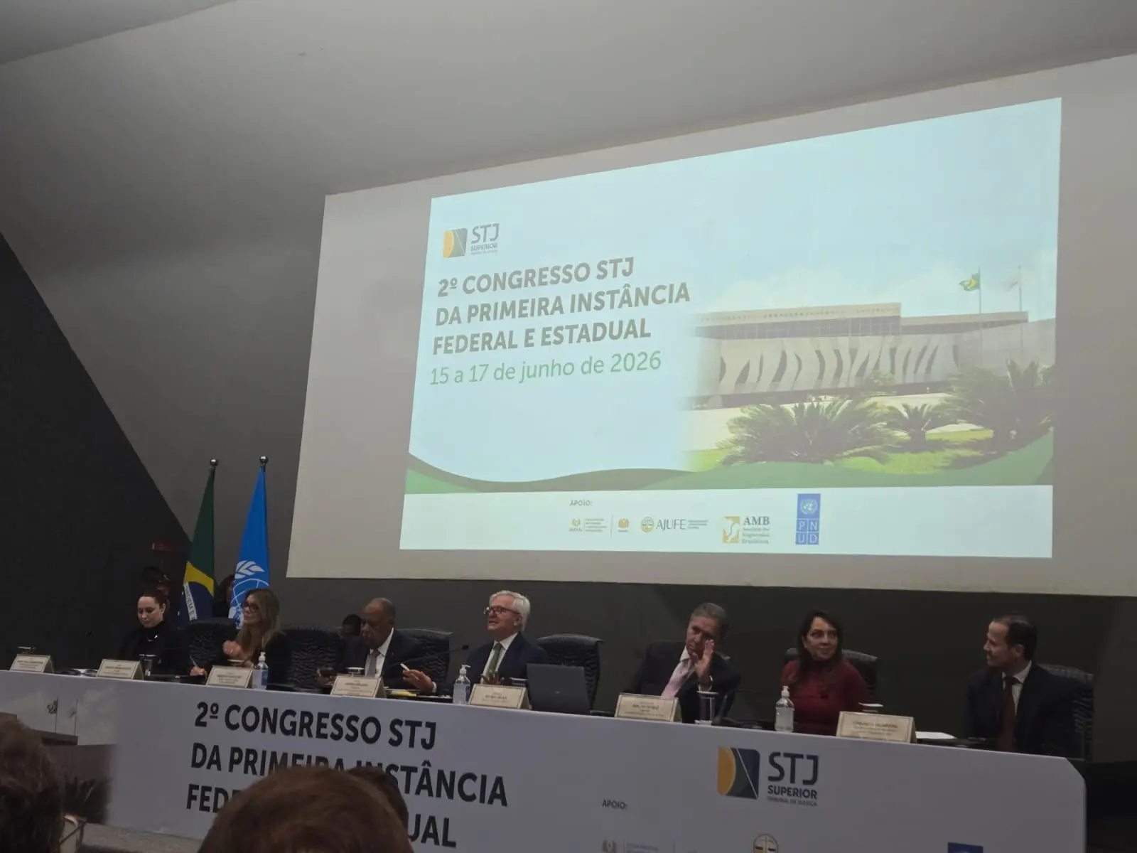 Sete pessoas compõem a mesa de um auditório no 2º Congresso STJ. Acima delas, um telão projeta o slide oficial do evento com imagem do tribunal.