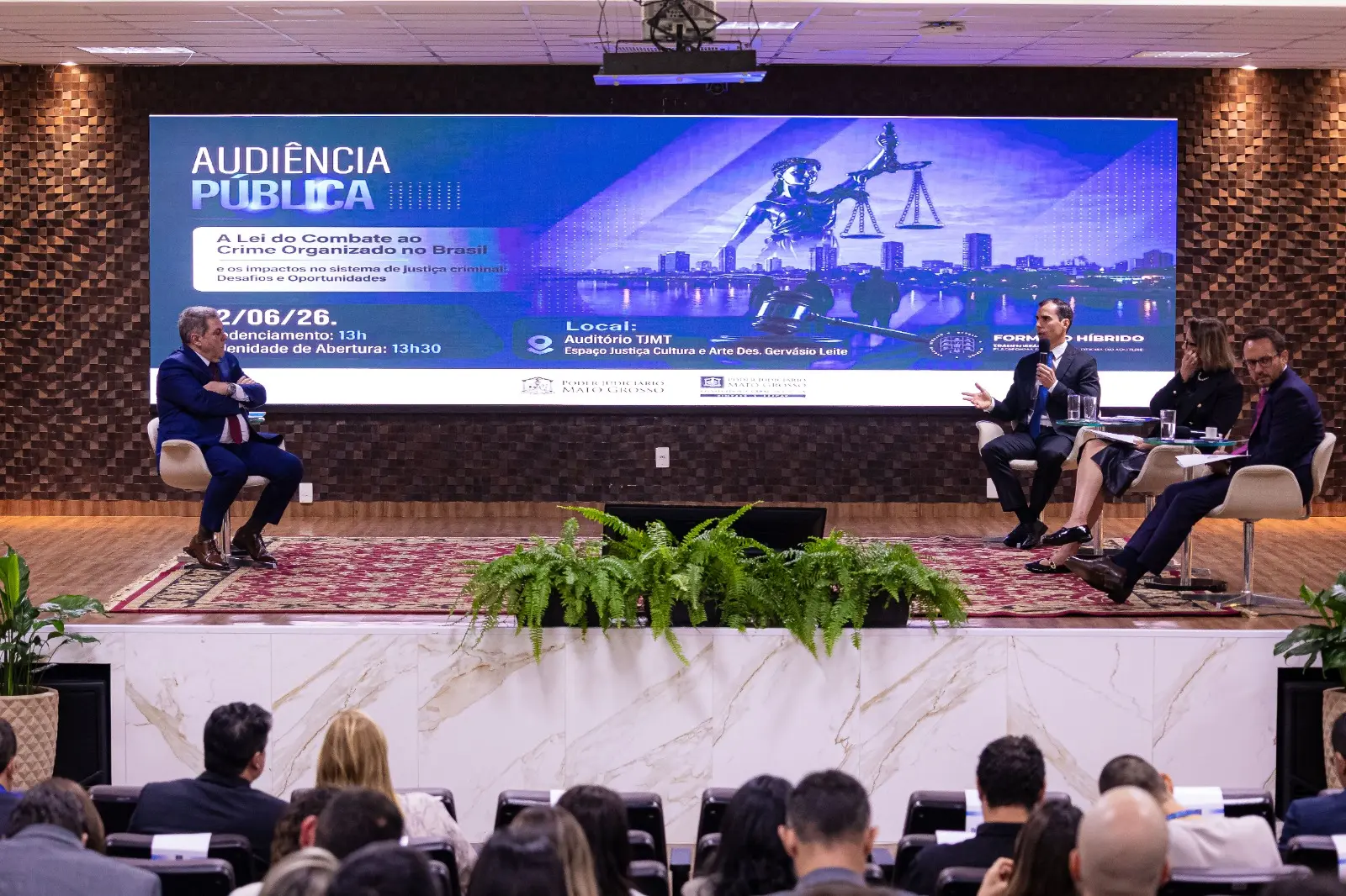 Palestrantes debatem no palco do auditório do TJMT sob um grande telão azul de 