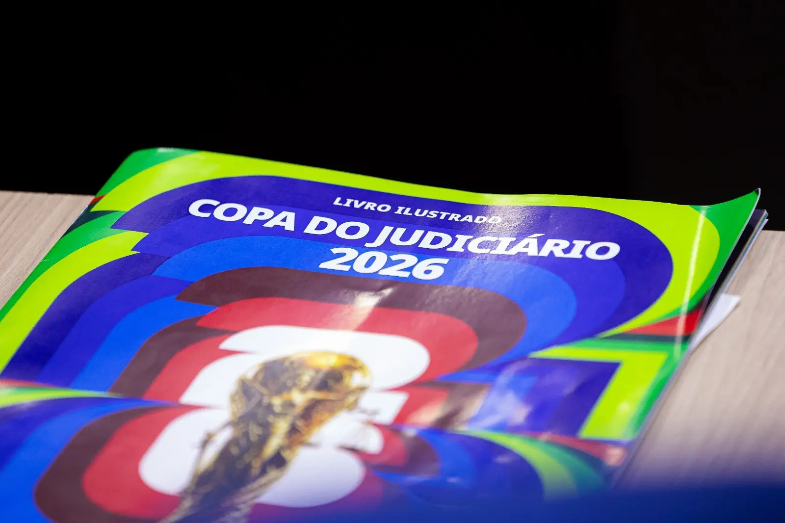 Álbum físico da Copa do Judiciário 2026 apoiado sobre uma mesa.