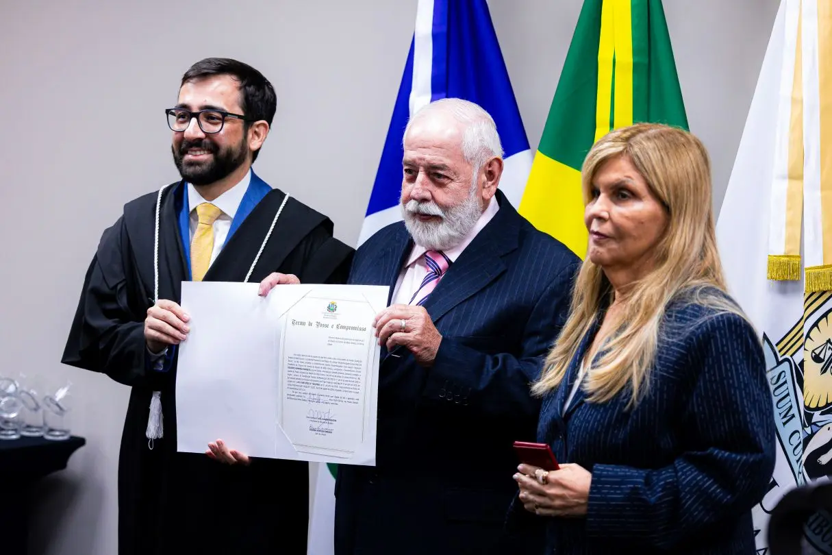 Foto horizontal que mostra, da esquerda para a direita, o juiz Eduardo Henrique Minosso, o presidente e a vice-presidente do TJMT, respectivamente, desembargadores José Zuquim e Nilza Maria Pôssas. Eles posam para foto mostrando termo de posse e carteira funcional do juiz.